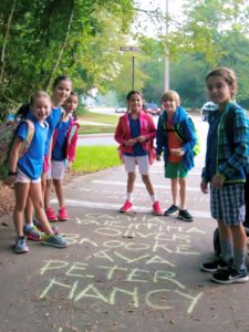 Students write their names on the sidewalk after walking to school.