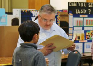 A volunteer judge listens intently to a student explain his project at the CB&I Junior High Science Fair.