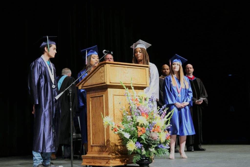 Four high school graduates stand at a podium.