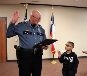 A little boy is sworn in as an officer by a police chief.