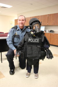 An officer stands with a little boy who is wearing SWAT gear.