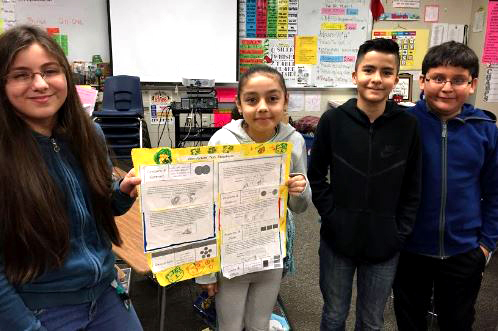 four students proudly hold up their science project