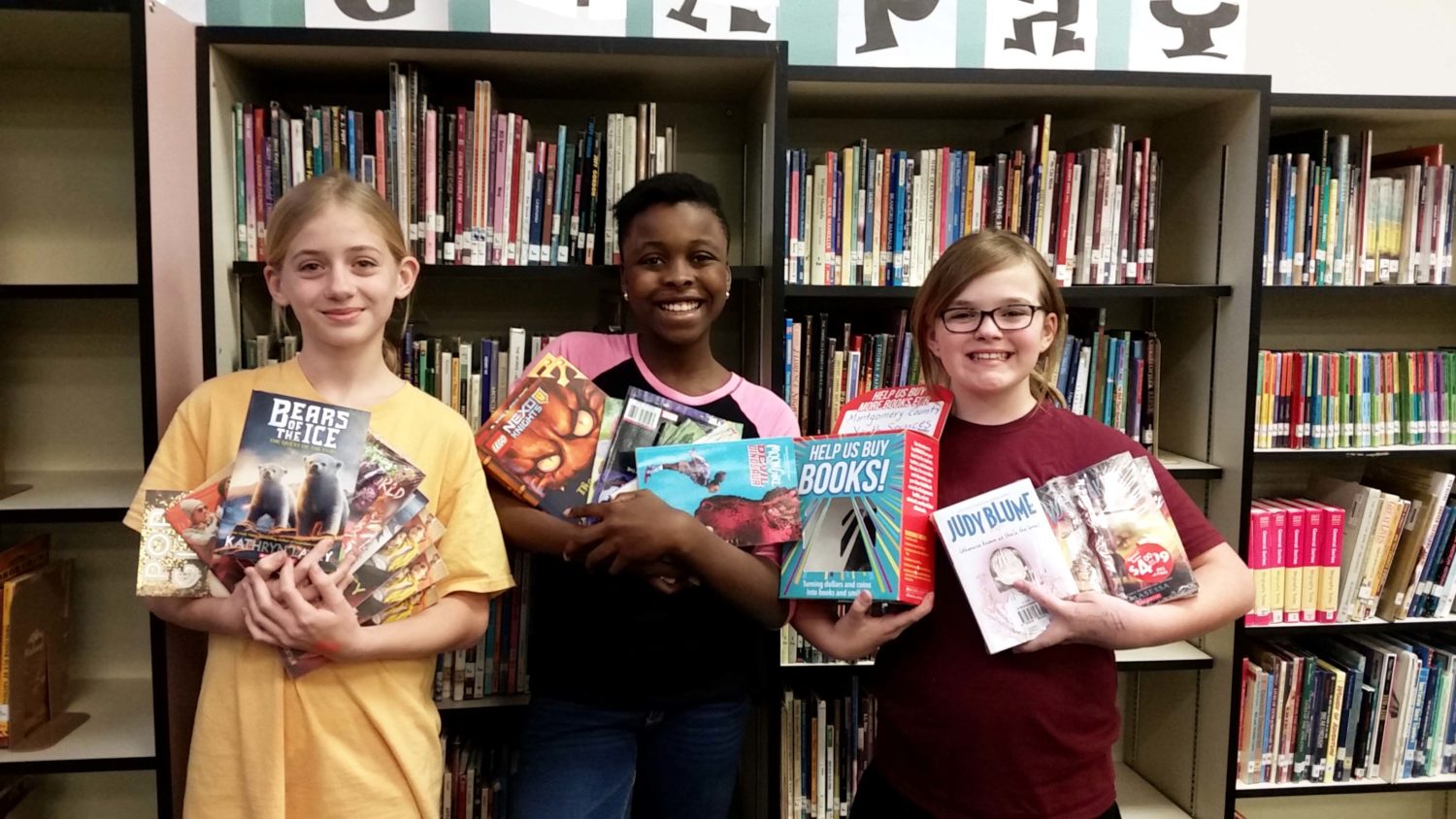 three students hold up books they have collected during their book drive