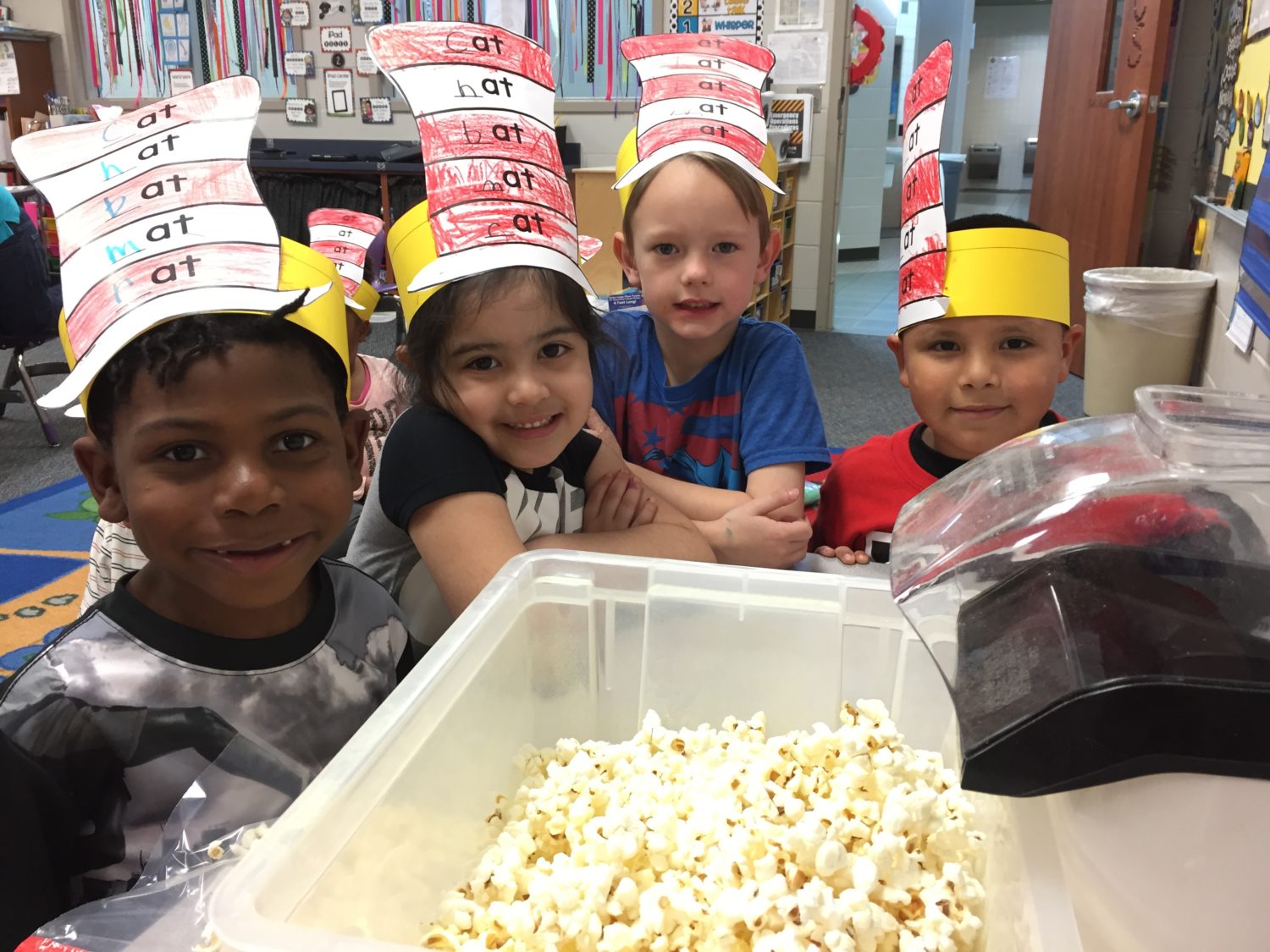 four students pose for a picture in front of a tub of popcorn made to celebrate Dr. Seuss birthday