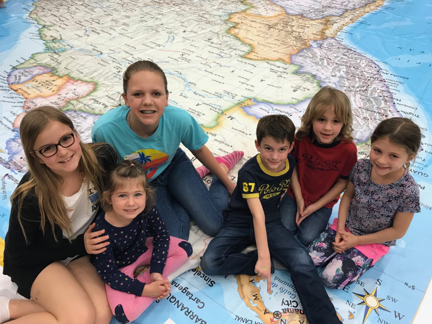 a group of six children sit on top of a map of the world and smile for a picture