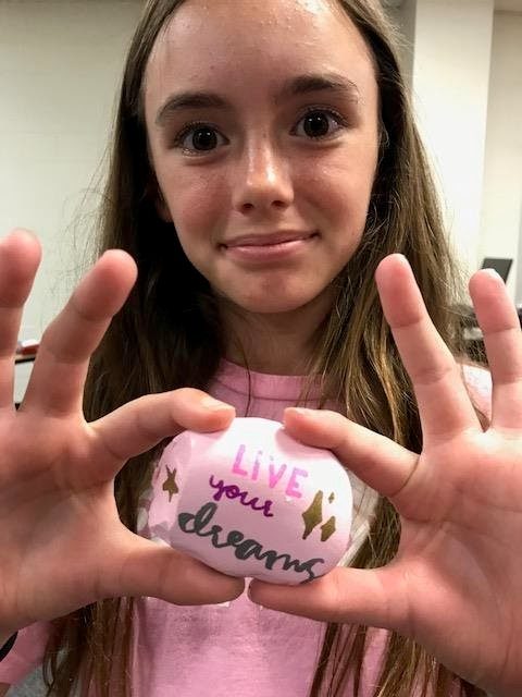 "a student holds up a rock she decorated for the school's kindness matters garden"