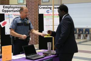 A police officer hands an application to a job interviewee.