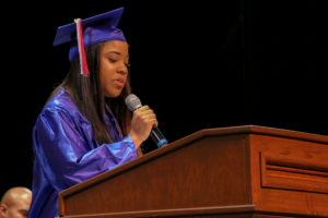 A woman in a cap and gown speaks at a podium.