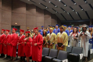 A group of high school graduates stand in an auditorium.