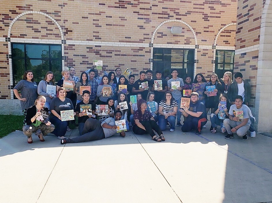"a group of kids pose with books outside of their school"