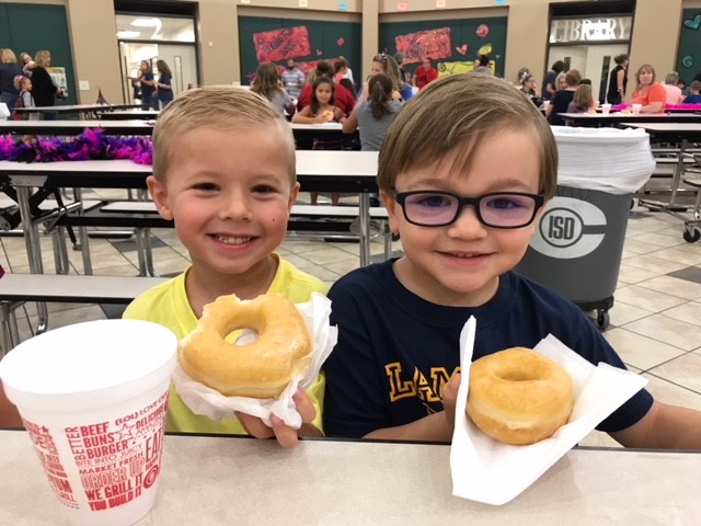 "two boys smile while holding donuts"