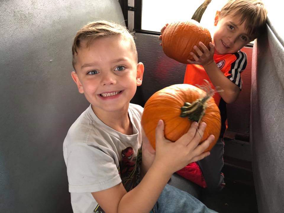"two boys hold pumpkins"
