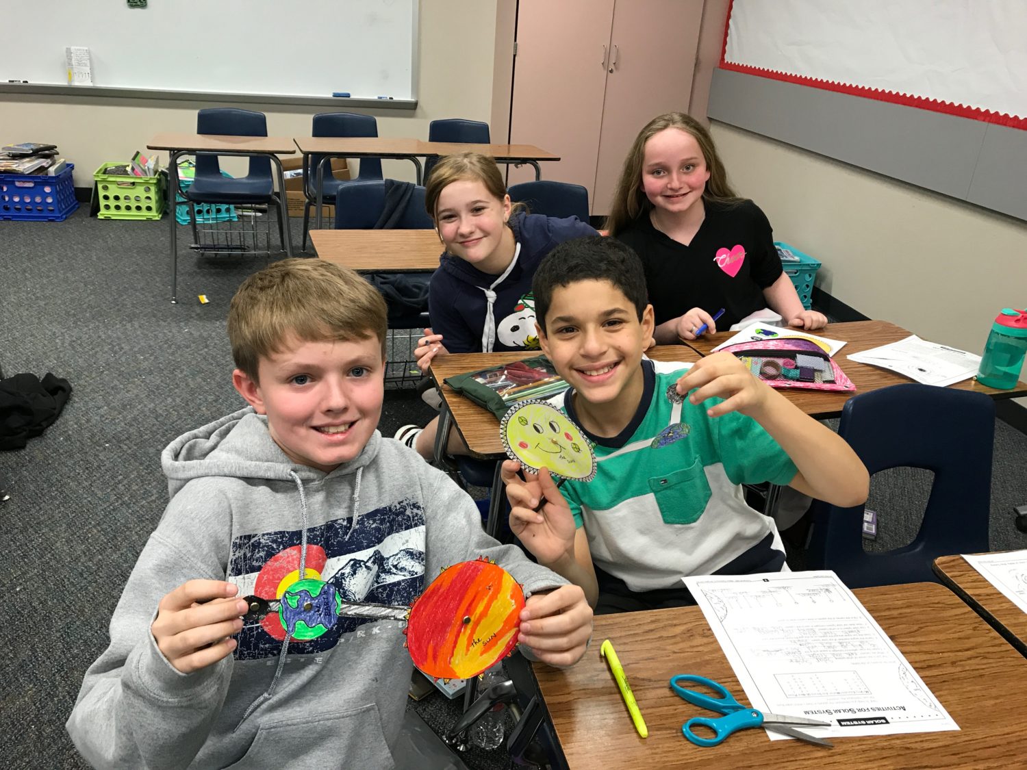 "four students hold up their solar system creations"