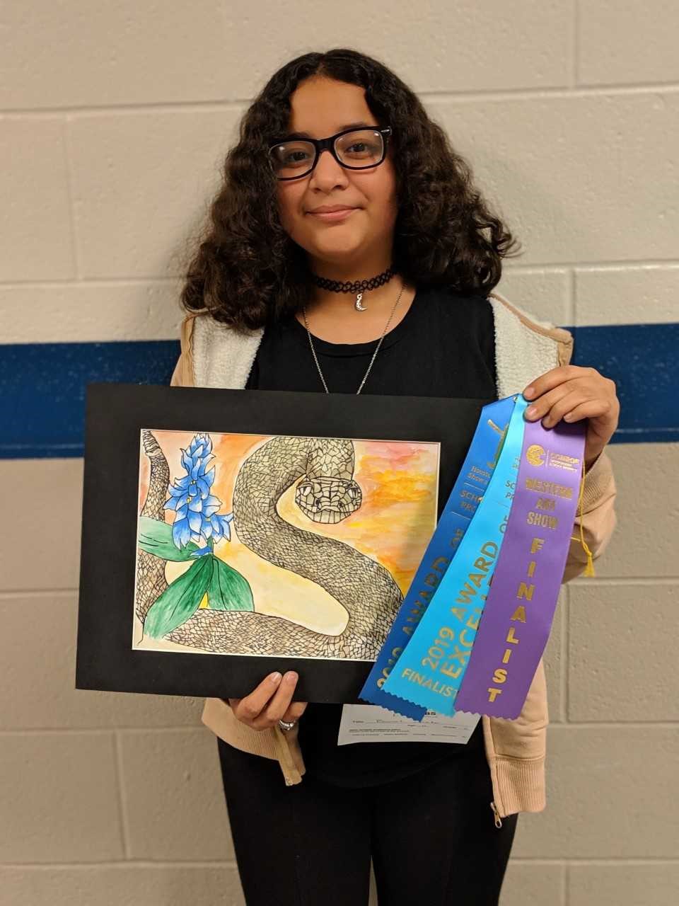 "a student holds up artwork and ribbons"