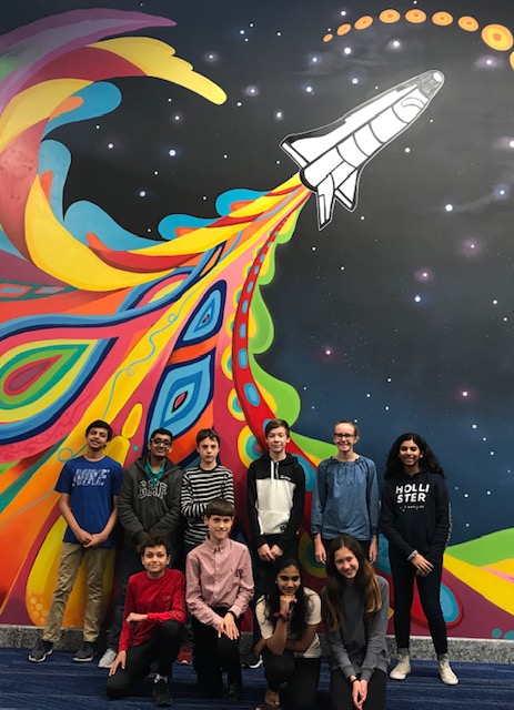 "students pose in front of a rocket mural"