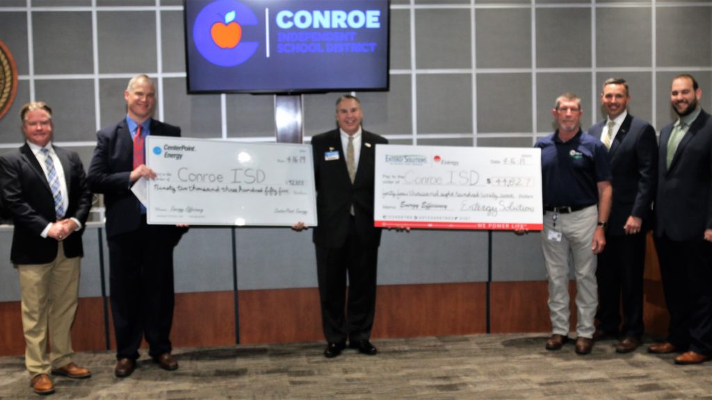 Men in suits pose with two large checks.