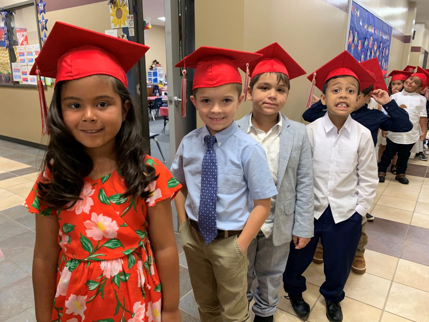 "children in graduation caps wait in a hall"