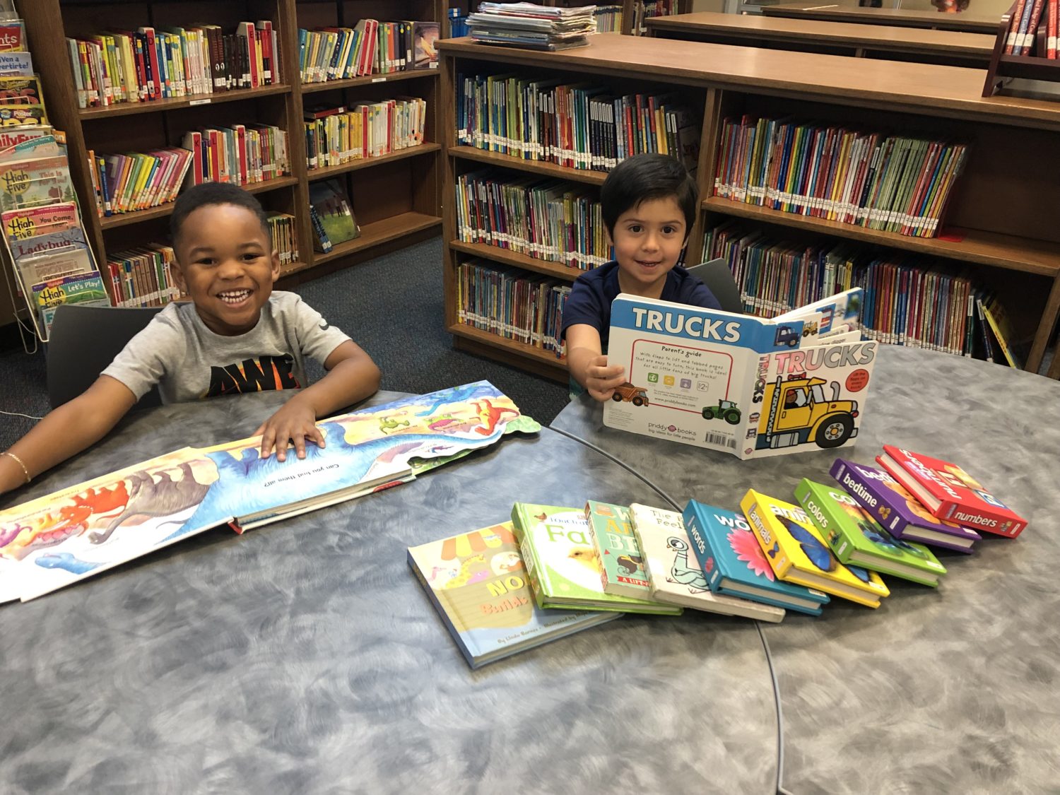 "two boys sit at a table with library books in their hands"