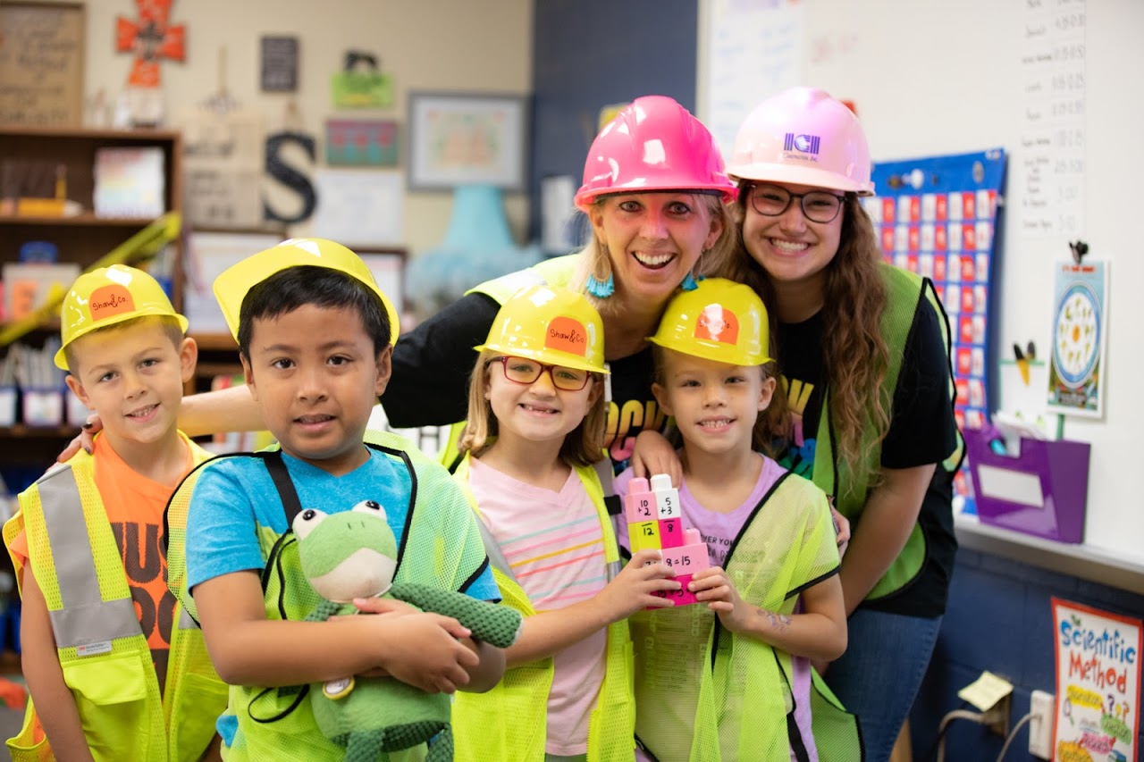 "students with hardhats hold up building blocks with math problems written on them"