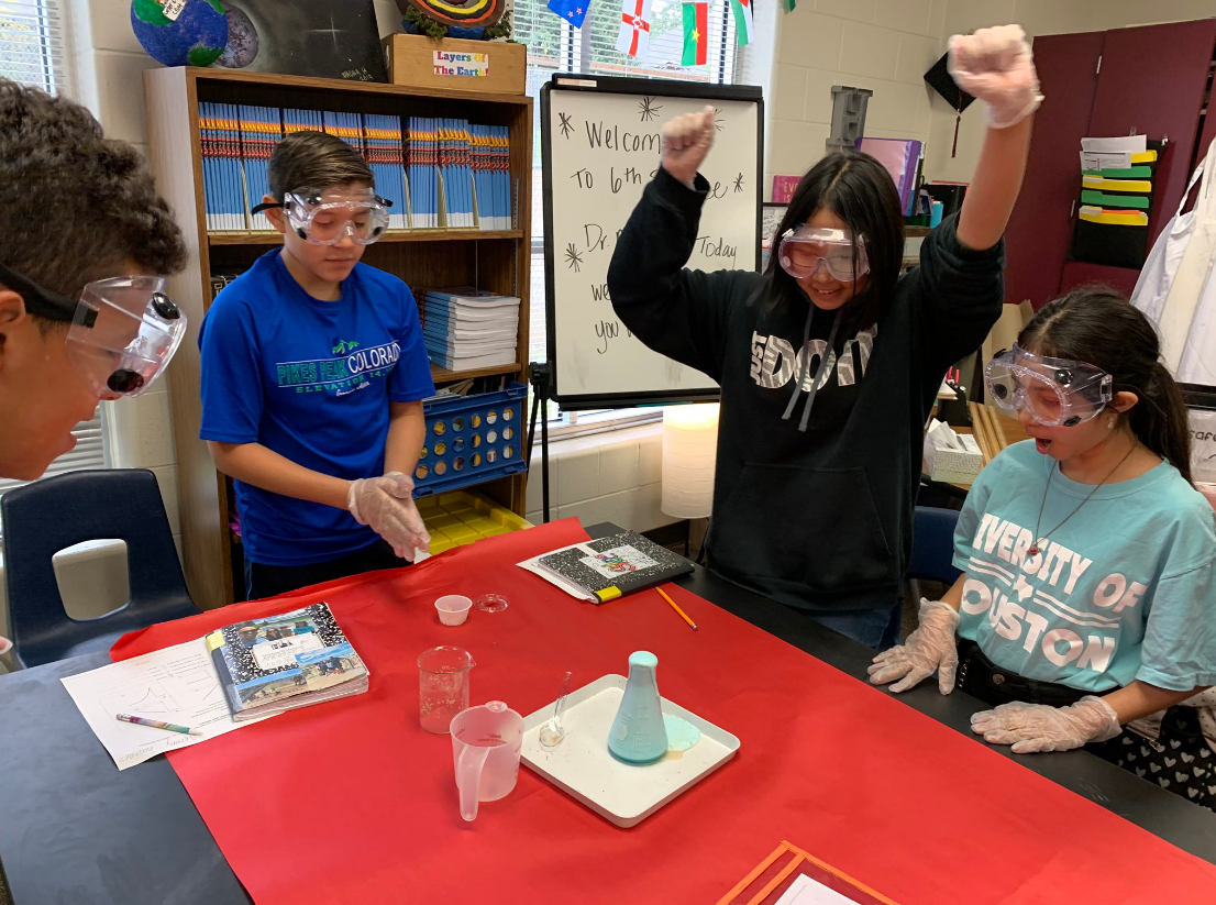"four students wearing goggles enjoy watching a chemical reaction"