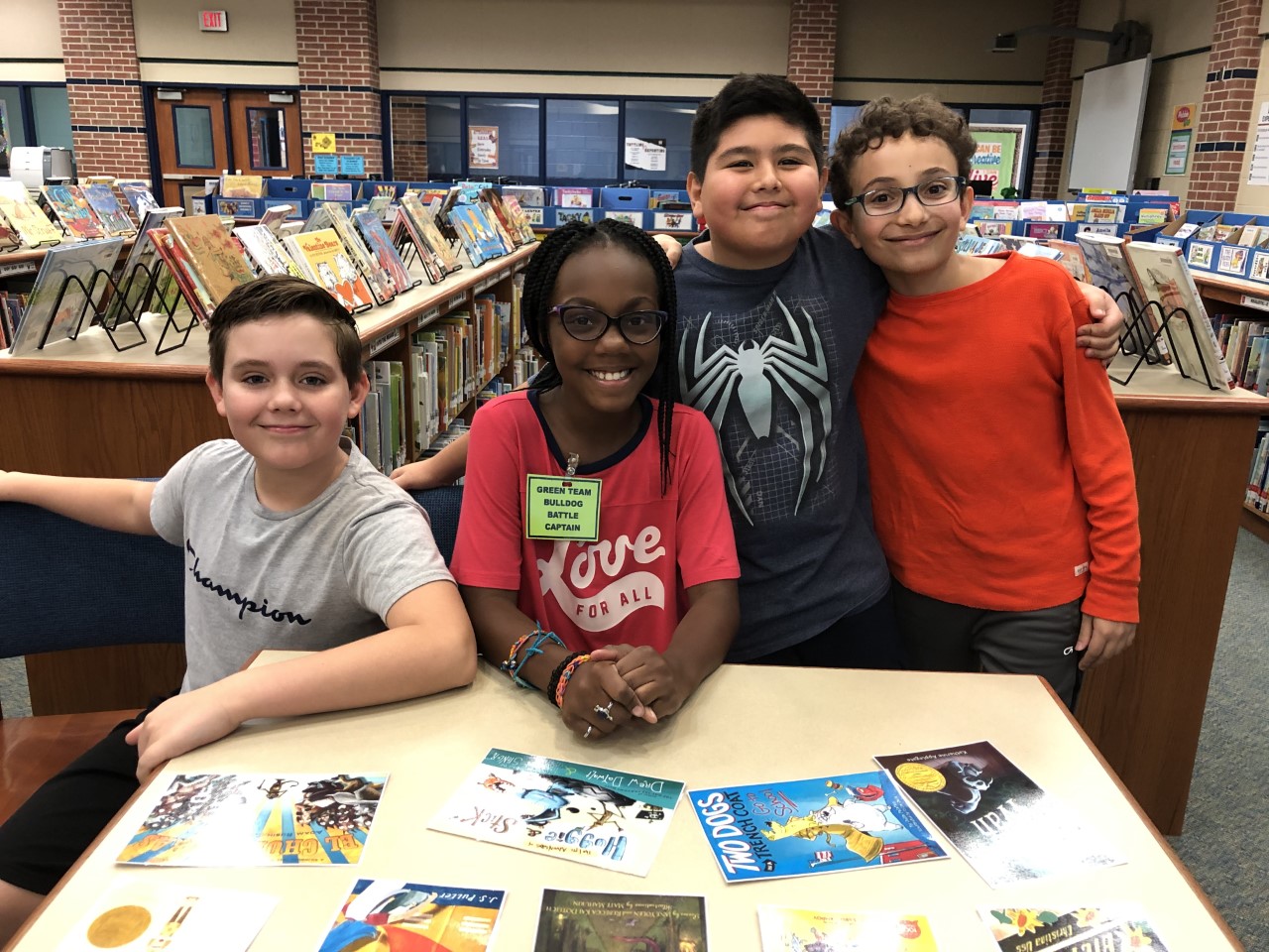 "four students smile for the camera in a school library"