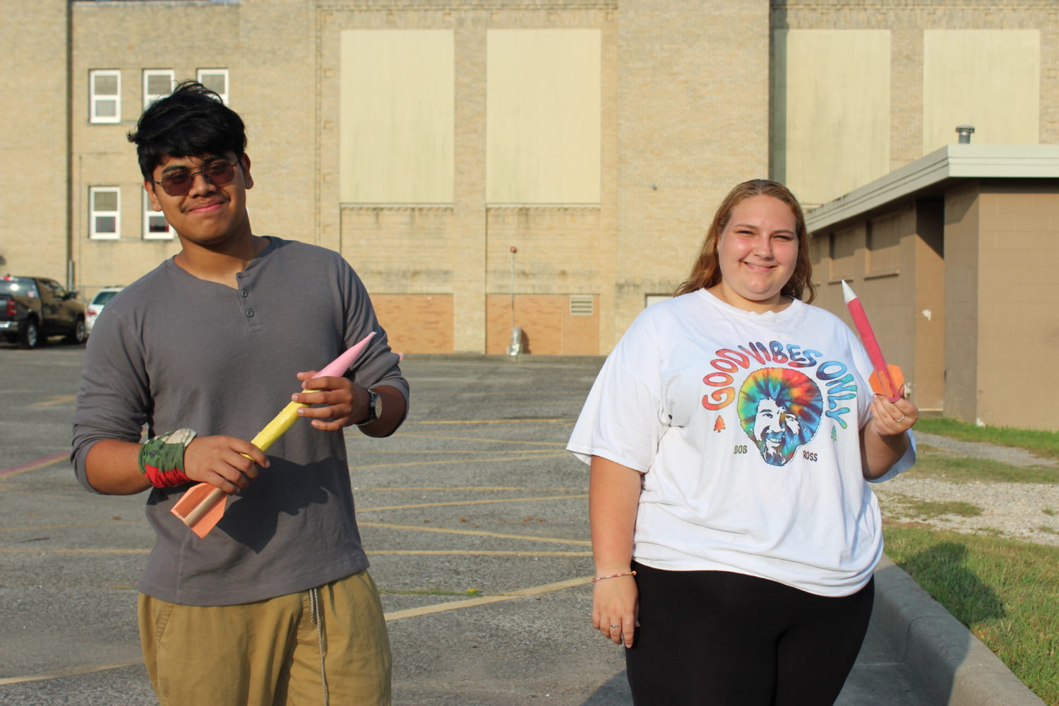 "two students hold up their homemade rockets for the camera while smiling"