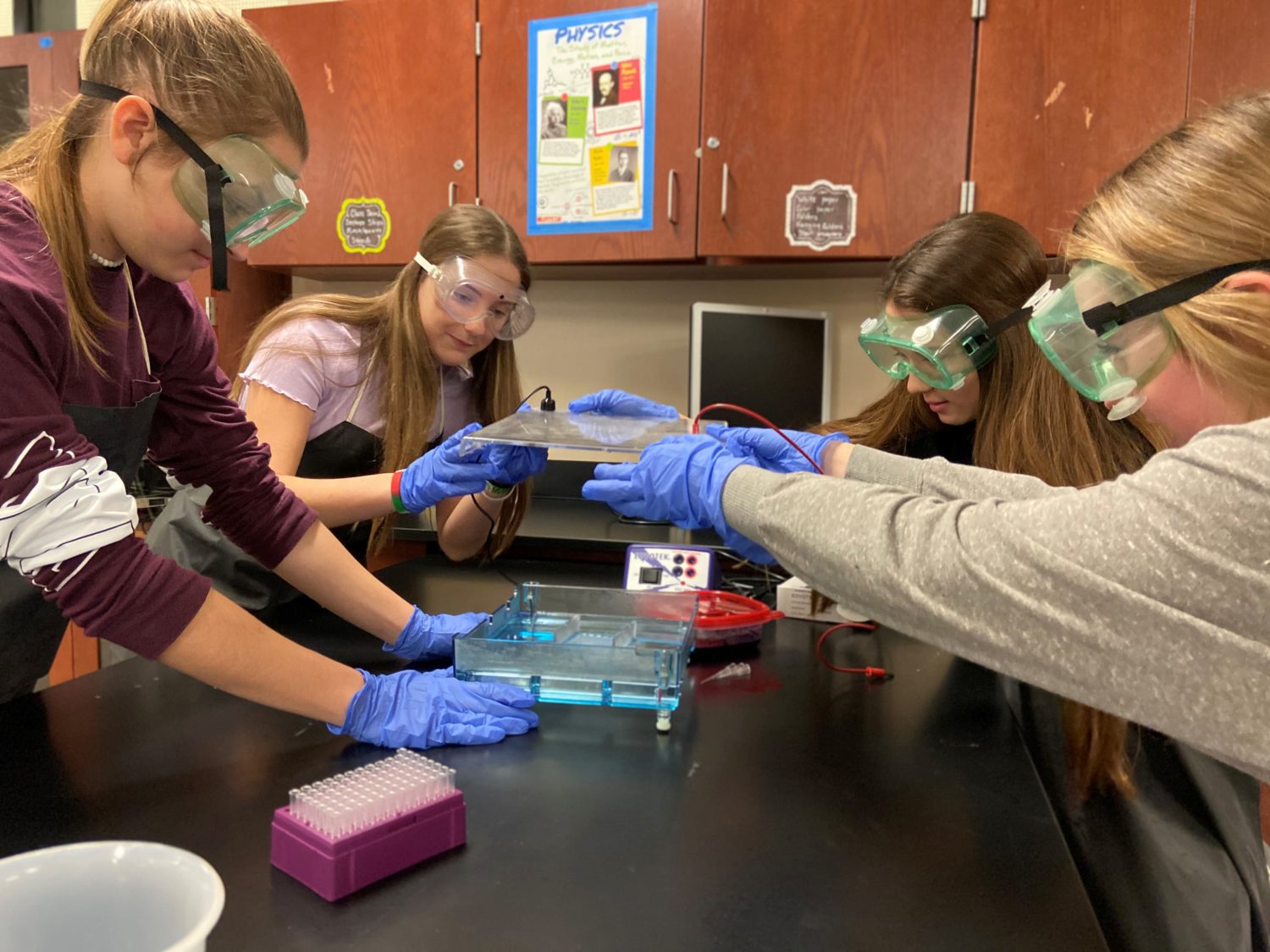 "four students in gloves and goggles work in a science lab"