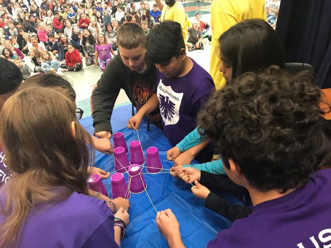 "a group of students dressed in purple work together during a team challenge"