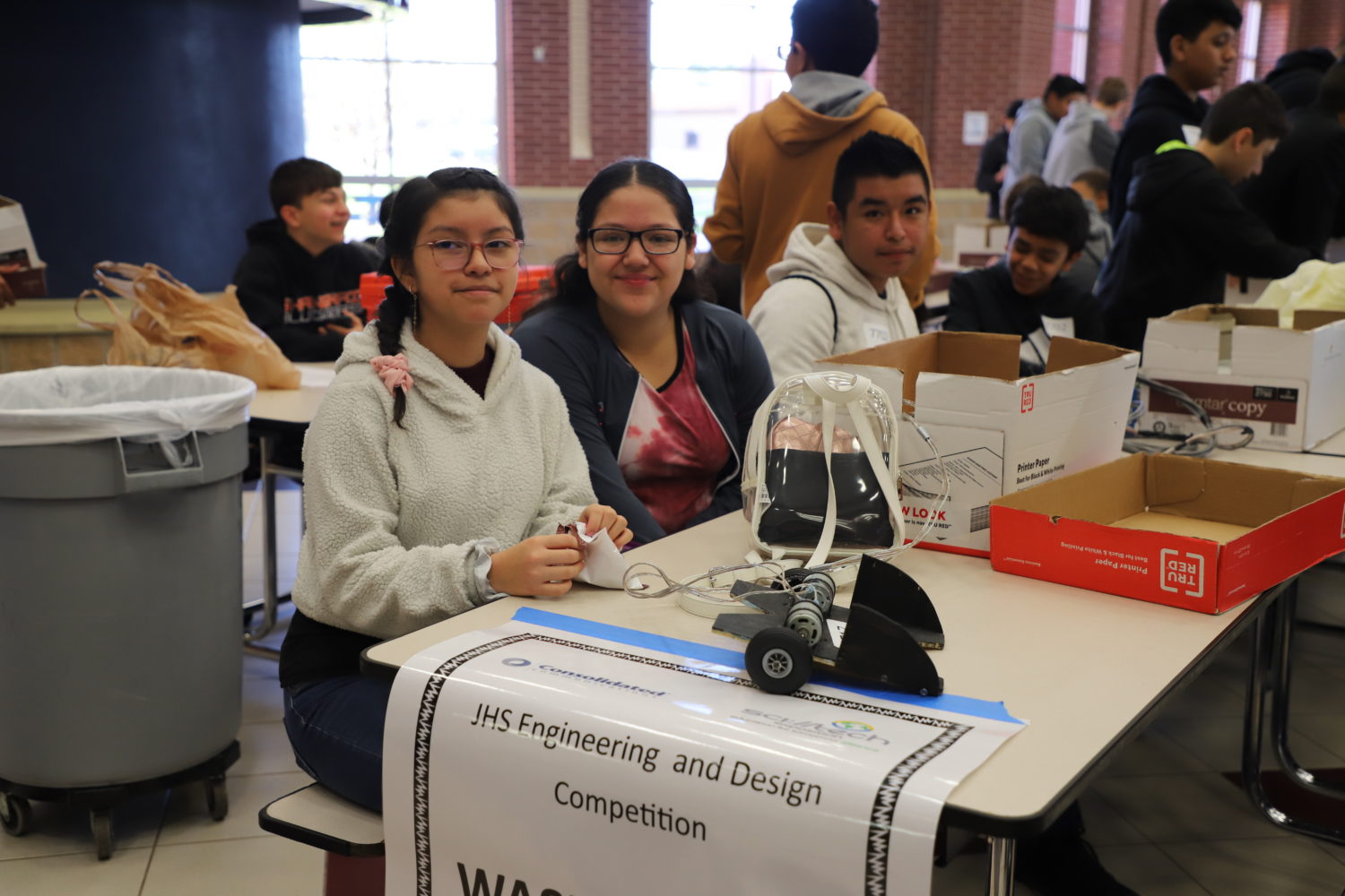 "three students with robotic components sit at a table"