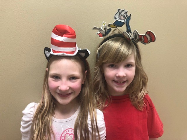 "two girls in Dr. Seuss headbands smile"