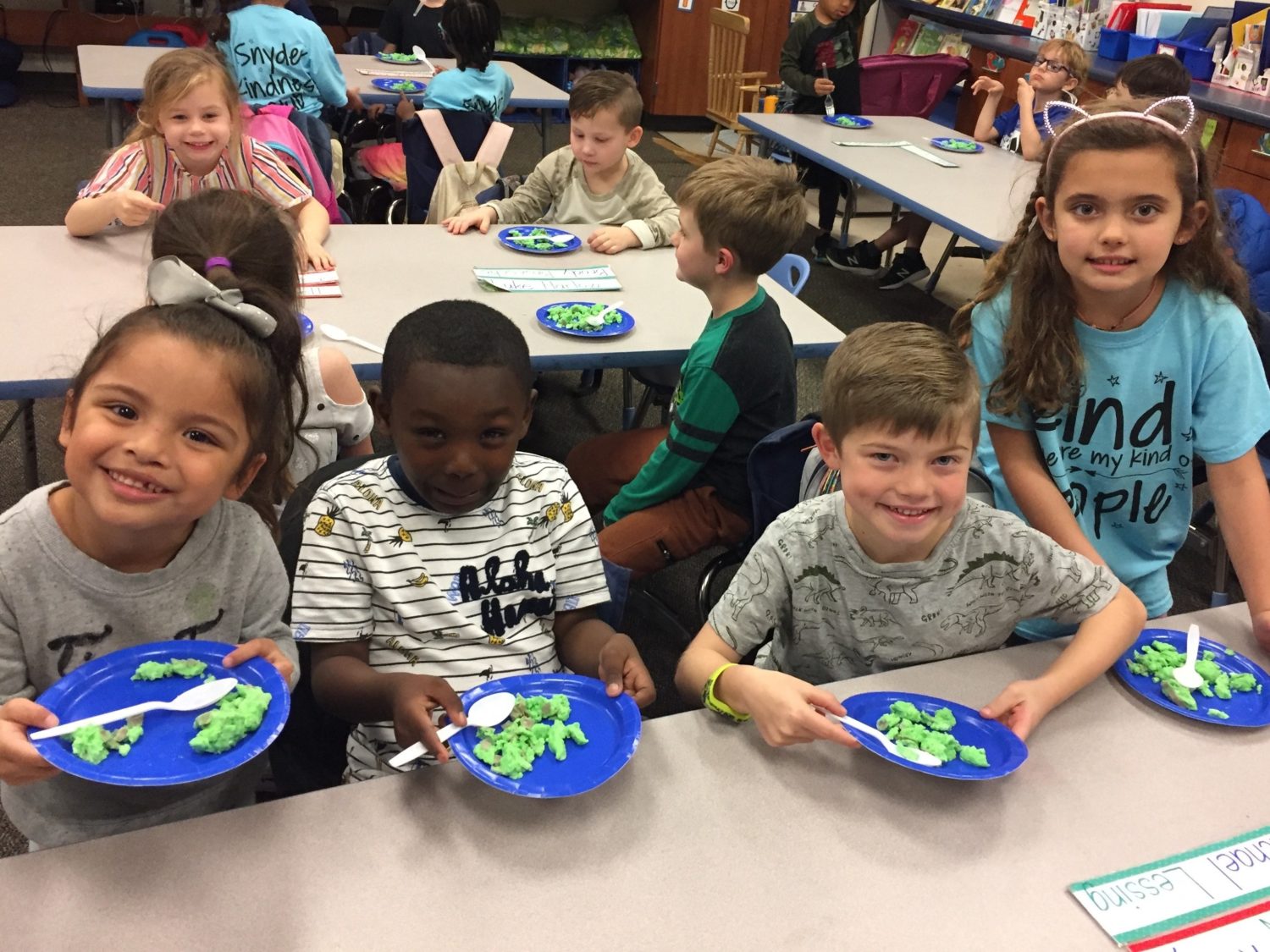 "four children sit at a table with green eggs and ham on their plates"