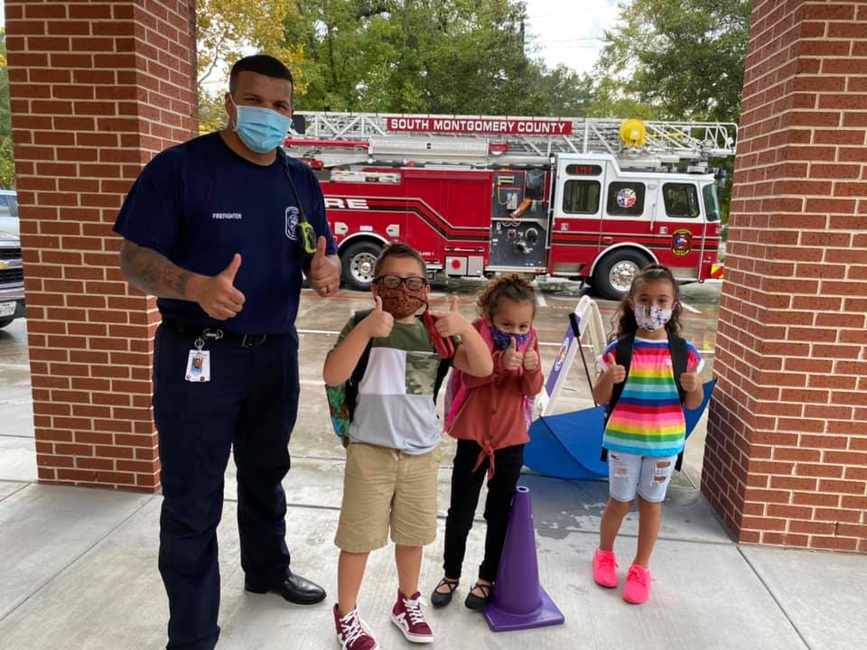 "three students stand with a firefighter in front of a fire truck"