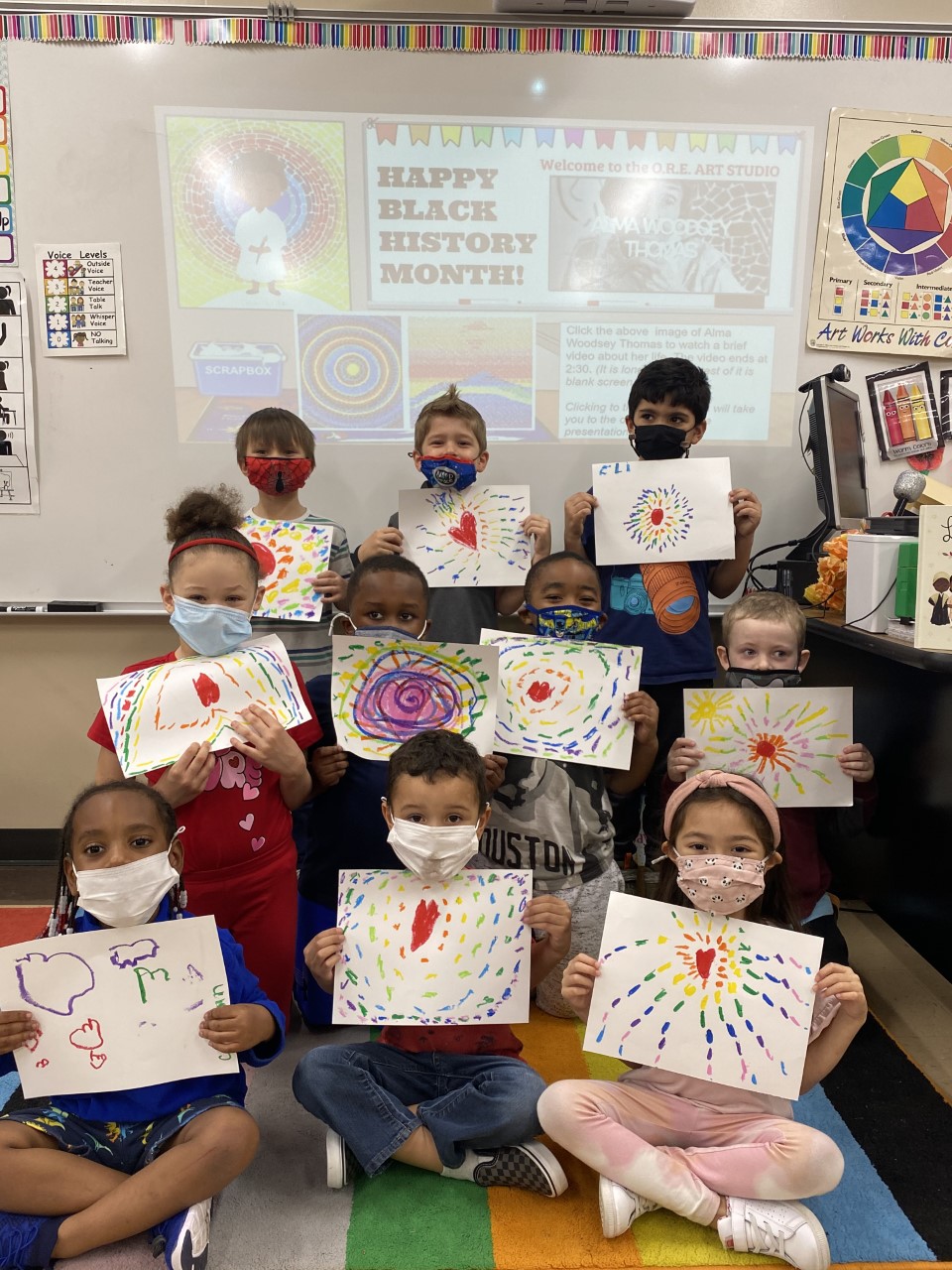 Students smile while holding their art work.