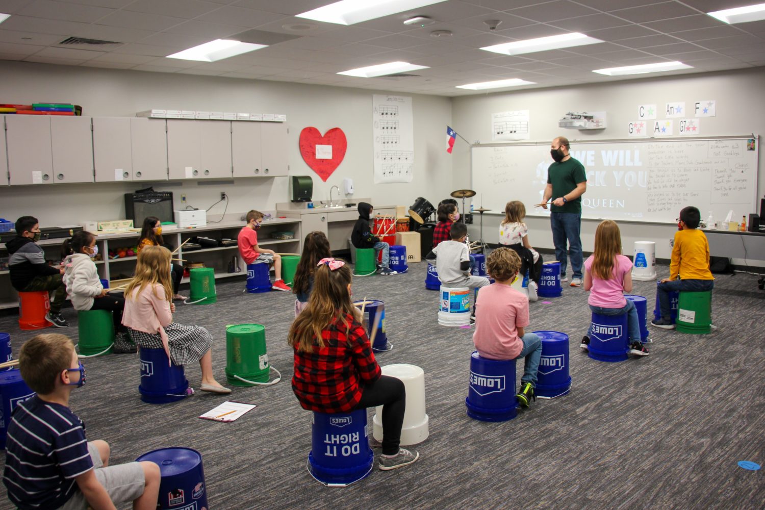 A group of students use buckets as drums in music class.