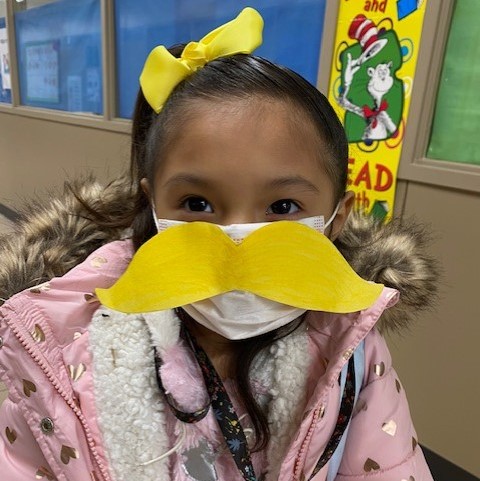 A student smiles for the camera while wearing a paper mustache.