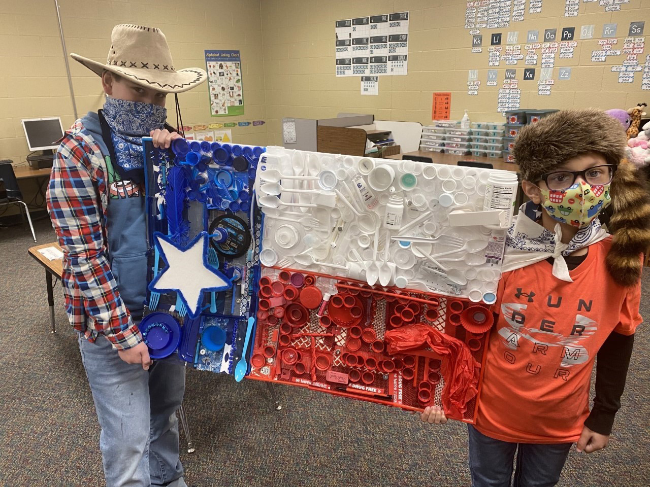 Two students smile while holding a Texas flag made from recycled materials.