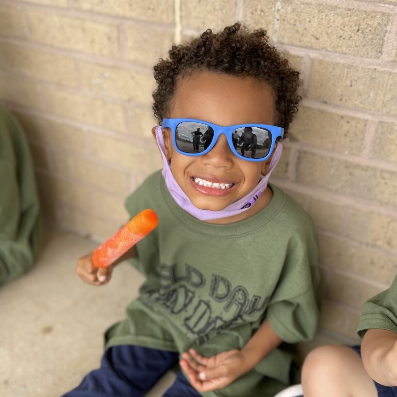 A student smiles for the camera while eating a popsicle.