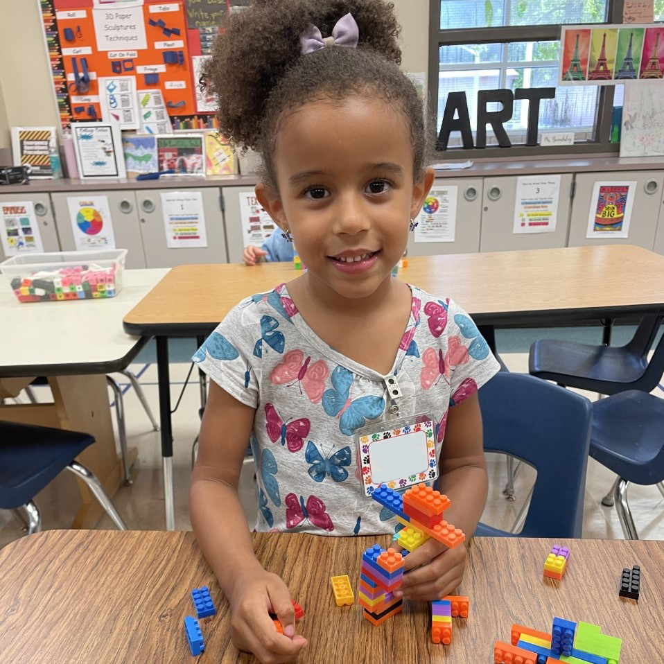 A student smiles for the camera while using building blocks.