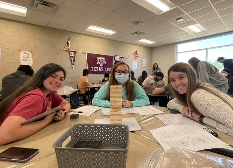 Three students smile for the camera while playing Jenga.