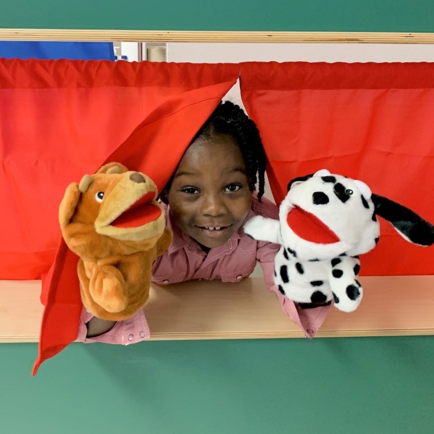A student smiles for the camera while holding two puppets.