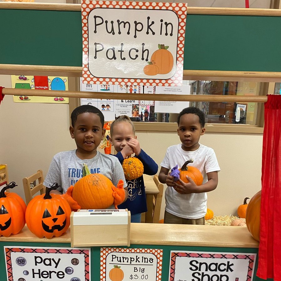 Three students smile while holding pumpkins.