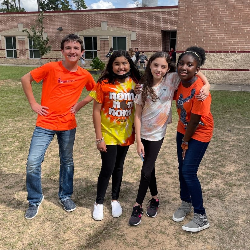 Four students smile for the camera while wearing orange shirts.