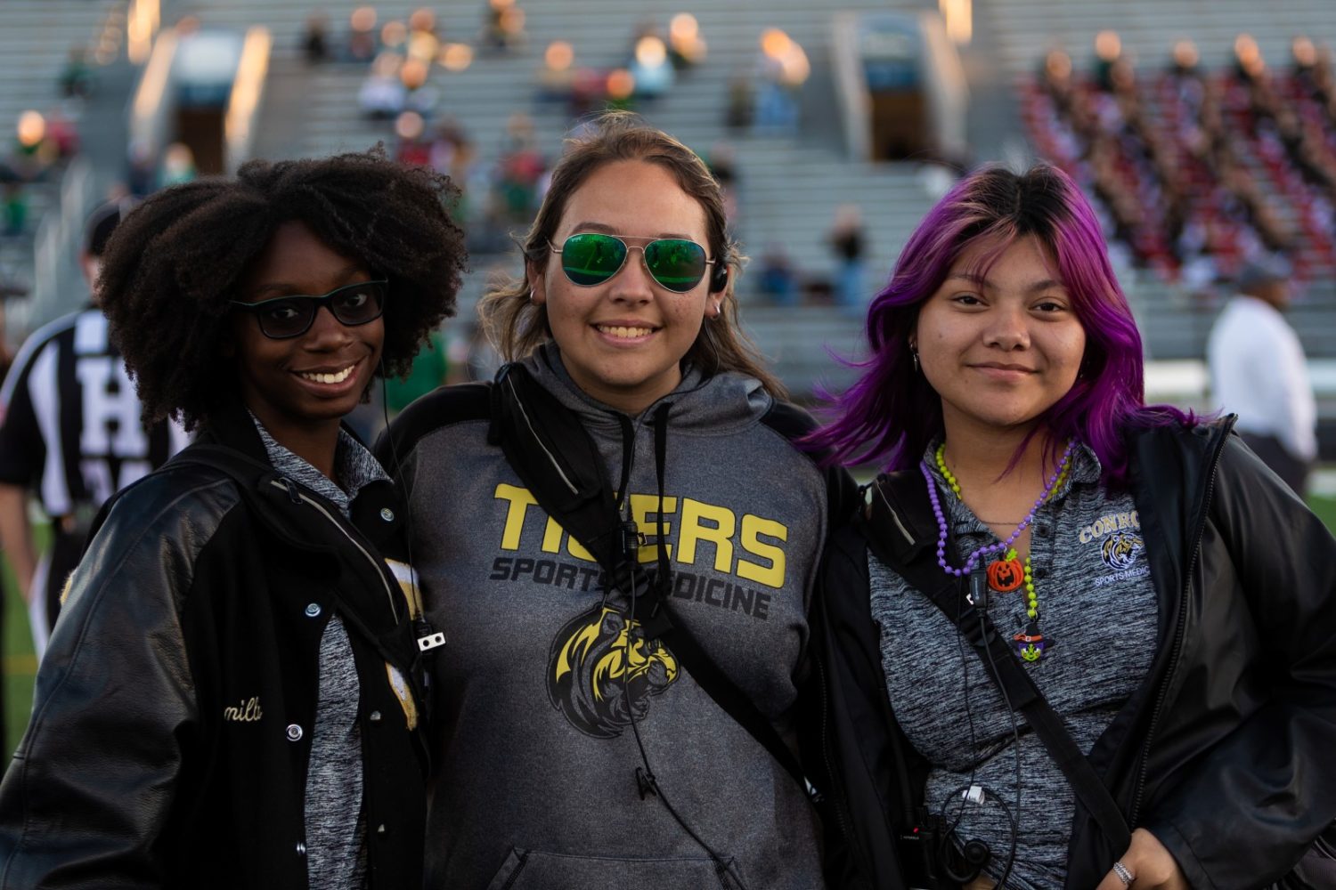 Three student trainers smile for the camera at a football game.