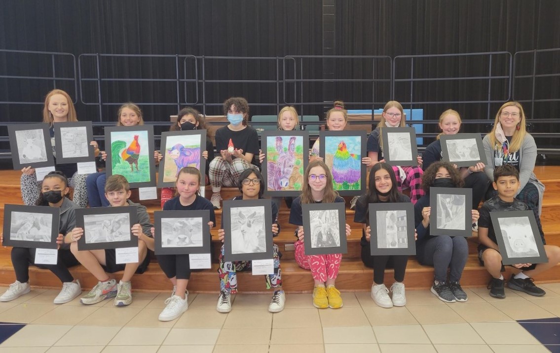 A group of students smile with their artwork.