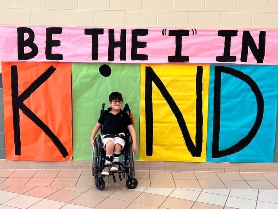 A student smiles in front of "kind" wall art.
