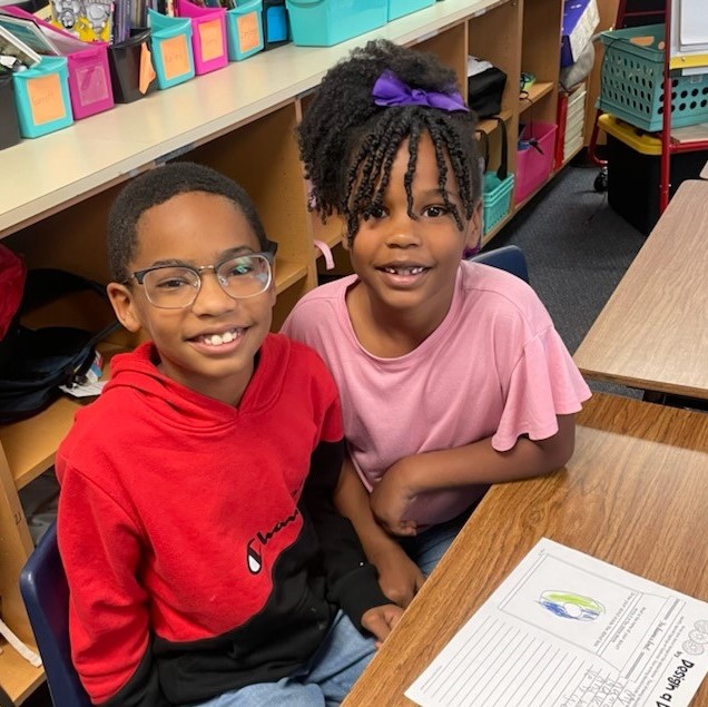 Two students smile for the camera while working together.
