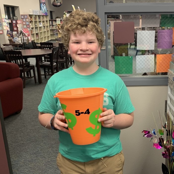 A student smiles with a bucket of pennies.