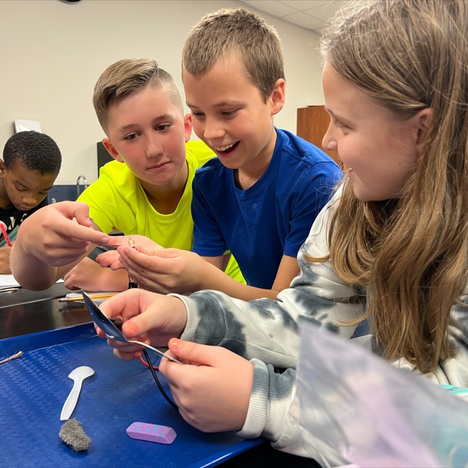 Students at Tom Cox work together to make light bulbs glow using electrical conductivity.
