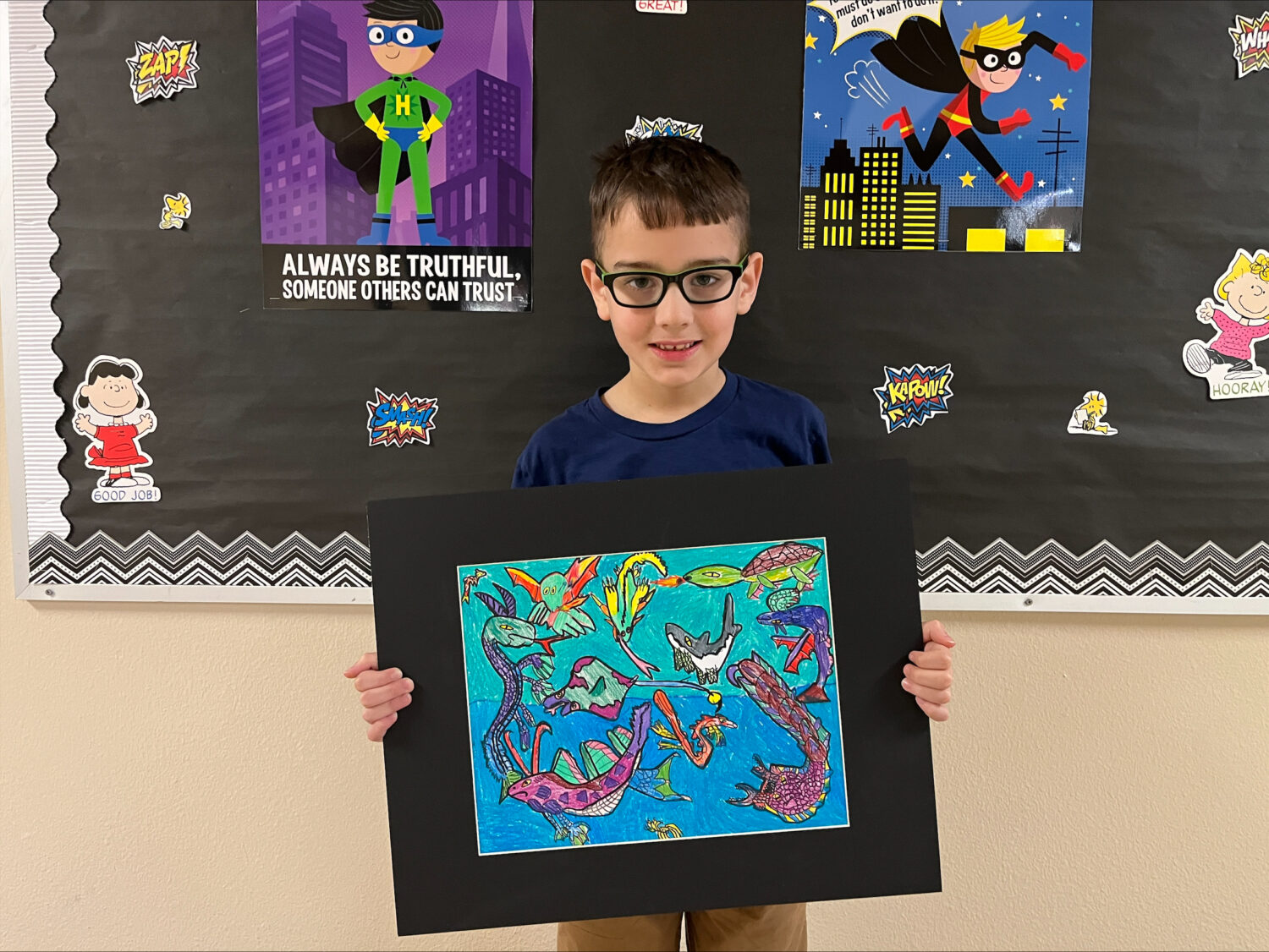 Boy with glasses holds up his artwork.